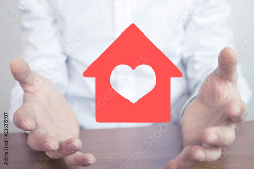 Hands holding red house with heart.