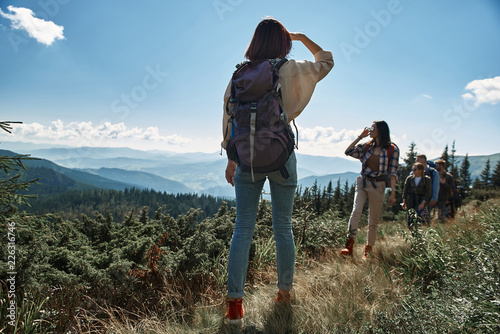 Rear view of a slim female tourist standing on the mountain hill while waiting for her friends photo