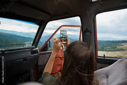 Rear view of a young delighted female traveler making shots of a beautiful scenery while travelling in the mountains by car