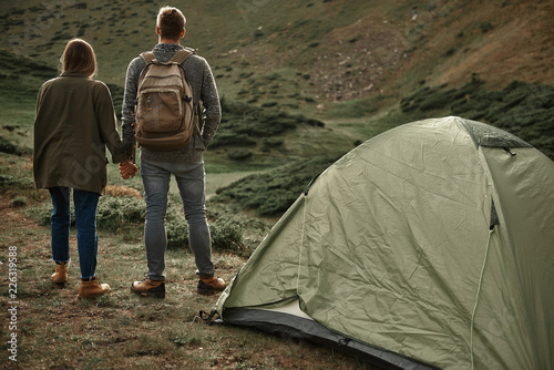 Life in mountains. Young romantic couple holding hands while standing near the mountain and admiring the view of the mountains