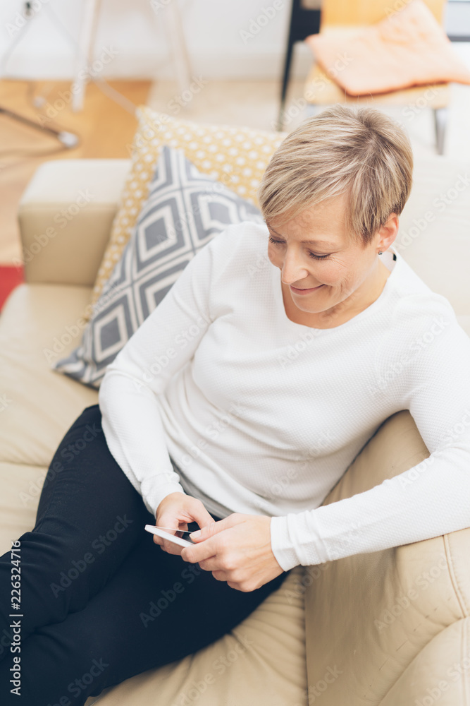 glückliche frau sitzt auf dem sofa und schaut auf ihr handy glückliche frau sitzt auf dem sofa und schaut auf ihr handy
