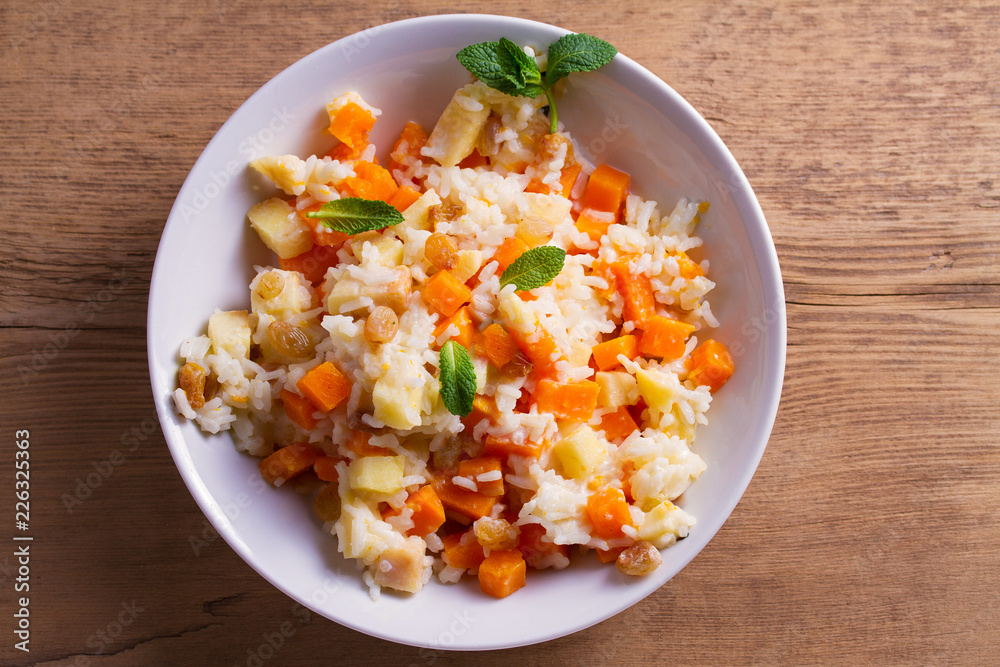 Rice porridge with pumpkin, apples and raisins in white bowl. Vegetarian diet dish of rice and pumpkin. Healthy food. overhead, horizontal Rice porridge with pumpkin, apples and raisins in white bowl. Vegetarian diet dish of rice and pumpkin. Healthy food. overhead, horizontal