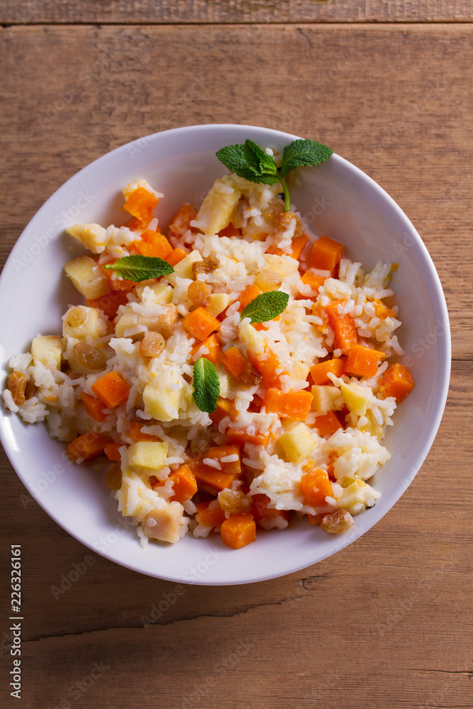Rice porridge with pumpkin, apples and raisins in white bowl. Vegetarian diet dish of rice and pumpkin. Healthy food. overhead, vertical Rice porridge with pumpkin, apples and raisins in white bowl. Vegetarian diet dish of rice and pumpkin. Healthy food. overhead, vertical