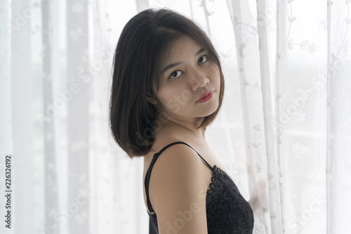 Asian young woman in black nightgown dress standing next to the window