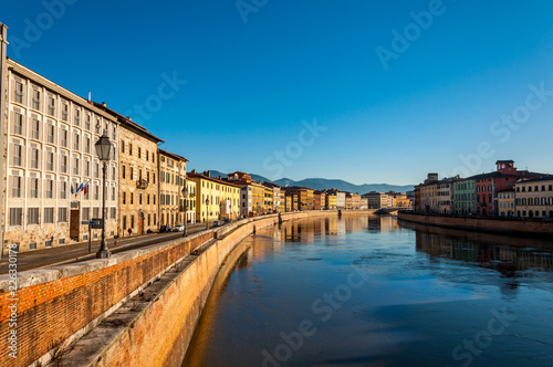 Beautiful morning on the river in Pisa, with small houses and blue sky