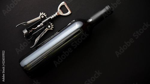 Red wine bottle and corkscrew on black matte background. Top view with copy space