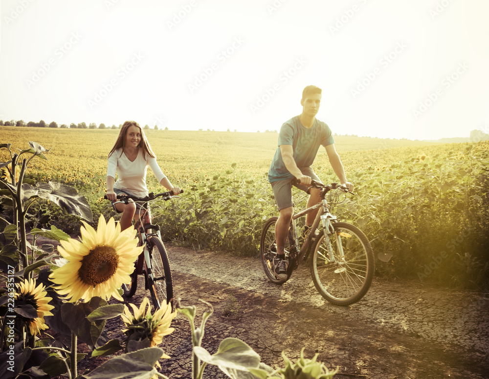Obraz premium Teen couple riding bike in sunflower field