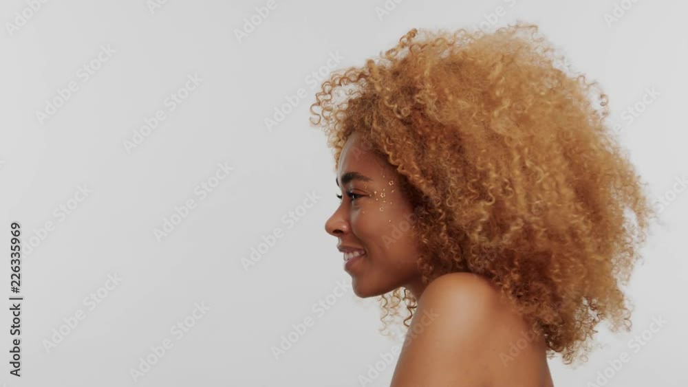 mixed race woman with millennial strobing skin and golden makeup stickers turning to a camera and smiling mixed race woman with millennial strobing skin and golden makeup stickers turning to a camera and smiling