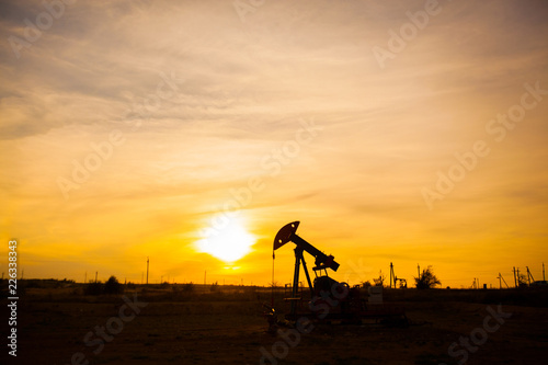 In the evening, the outline of the oil pump. The oil pump, industrial equipment. Oil field site, oil pumps are running. Rocking machines for oil production in a private sector.