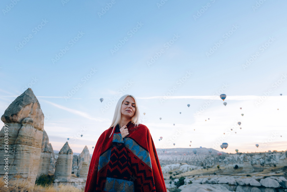 Naklejka premium girl in ethnic clothes at dawn watching the flight a lot of balloons fly over the valley of love