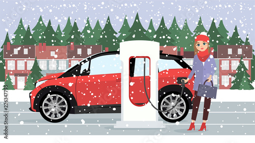 Woman charges an electric car at a charging station for electric vehicles. Winter time. Snow.
