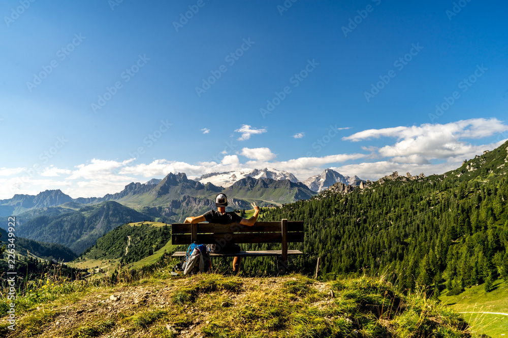 Wunderschöner Ausblick auf die  Berge in den den Alpen mit einer Person auf einer Bank im Vordergrund