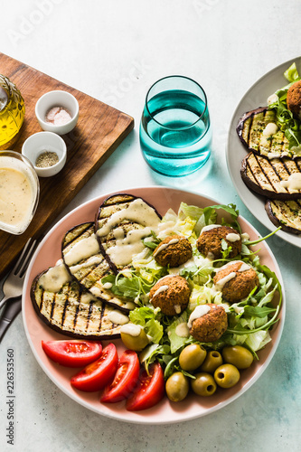 an appetizing dinner or lunch from a salad with tomatoes, grilled eggplants and legume falafel with sesame tahini dressing. Vegan healthy food for the whole family