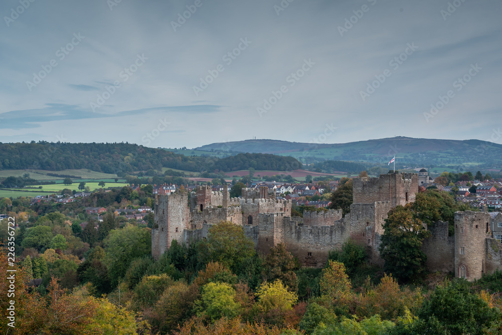 View across autumnal woodland to Ludlow Castle built by the Normans with the Clee Hills in the background.