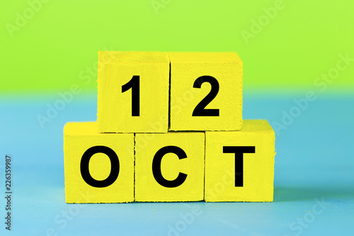 OCT 12, yellow cube calendar on blue wooden surface with copy space