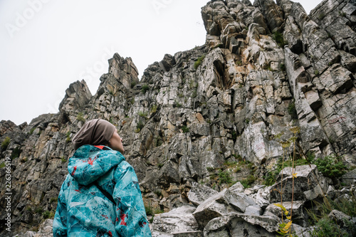 Two hikers staying on rock.Young female travelers on top of high stone wall observing mountain landscape sunny day holding walking poles with backpacks on bright sun shining on background