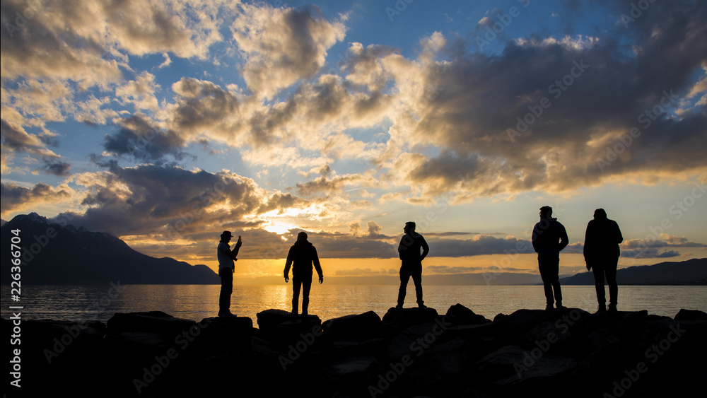 A traveller group silhouette take a photo with colorful sunset mountains background, lake Geneva, Montreax, Switzerland