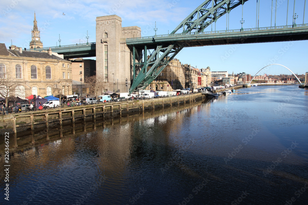 Naklejka premium The Tyne and Millenium bridges of Newcastle-Upon-Tyne with the busy sunday market taking place on the quayside