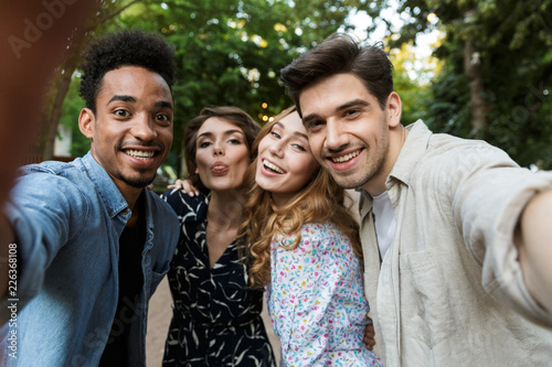 Young group of friends outdoors in park having fun take a selfie by camera.