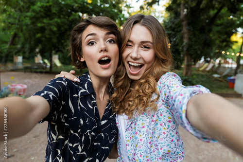 Young women friends outdoors in park having fun looking camera take a selfie.