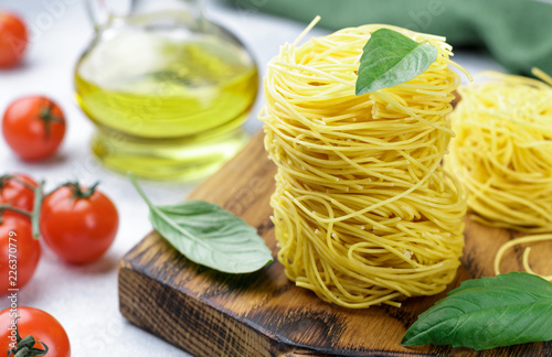 Raw Egg pasta nest - Homemade Capelli d'angelo, Angel's hair. Italian Cuisine. Ingredients for a delicious dinner. Basil, vermicelli, tomatoes, olive oil and spices on the table