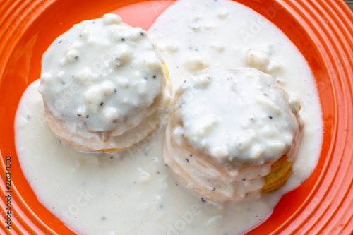 Two homemade biscuits smothered in sausage gravy set on an orange plate on the kitchen table for breakfast