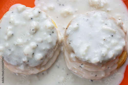 Two homemade biscuits smothered in sausage gravy set on an orange plate on the kitchen table for breakfast