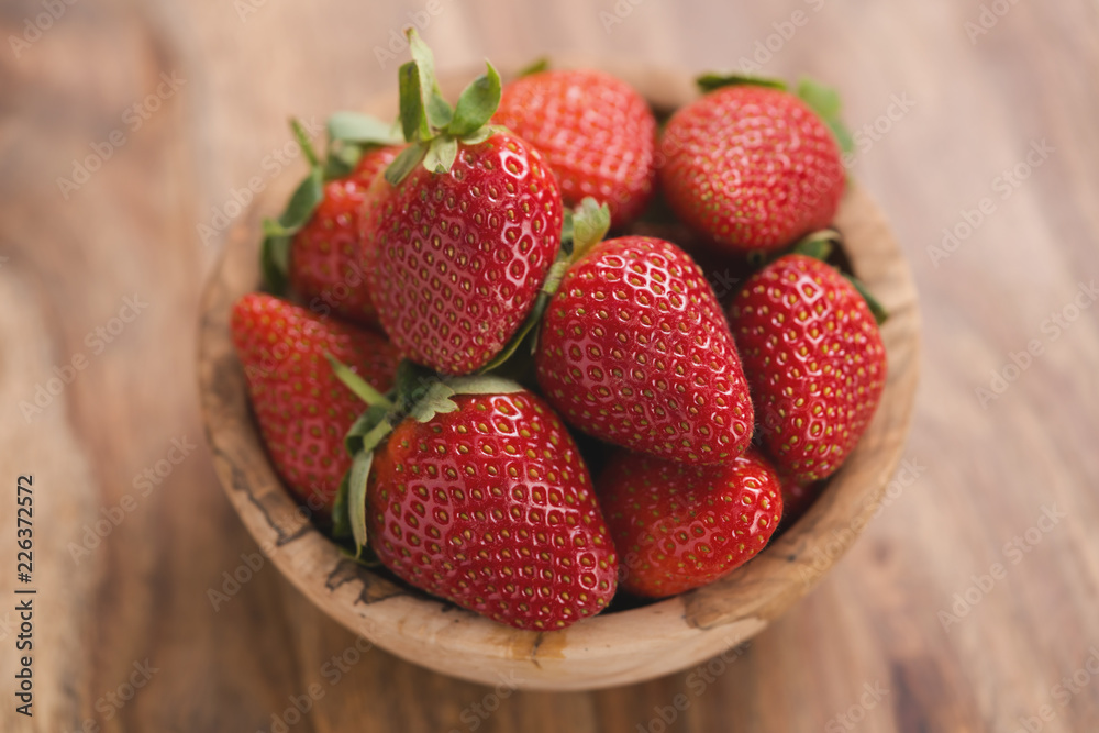 Ripe strawberries in wooden bowl on wood background from above Ripe strawberries in wooden bowl on wood background from above