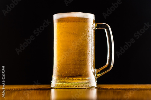 Frosty mug of beer close up on wooden table against black background.
