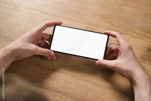 Fototapeta Naklejka Na Ścianę i Meble -  young man hands holding smartphone with blank white screen in landscape mode