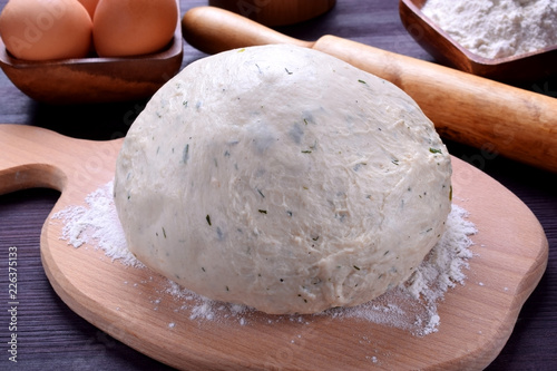 Yeast dough with herbs on a wooden board surrounded by the ingredients