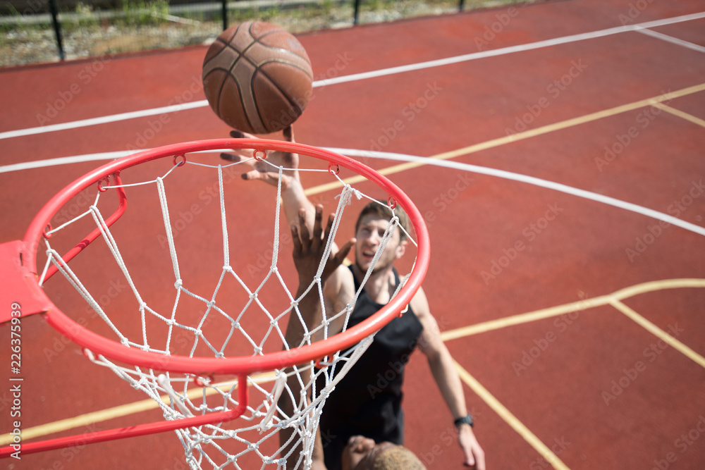 Obraz premium High angle portrait of young basketball player throwing ball in hoop and scoring on outdoor court lit by sunlight, copy space