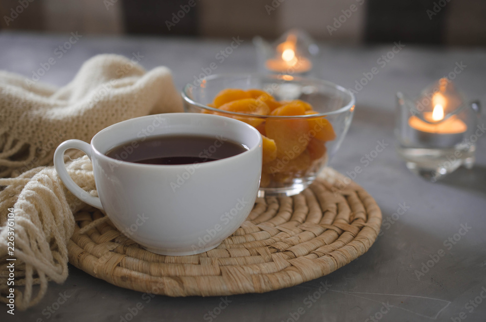 Cup of tea and dried apricots on a table, candles and knited blanket.