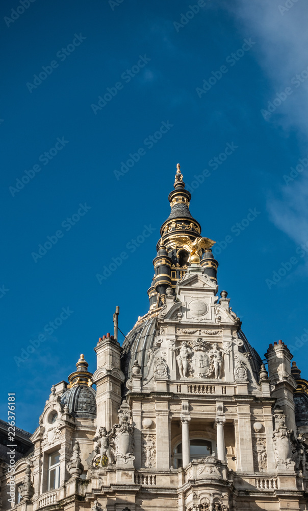 Antwerp, Belgium - September 24, 2018: White-gray facade on corner of Kipdorpvest and Leysstraat with blue sky as background. Golden eagle, town coat of arms fresco and statues.