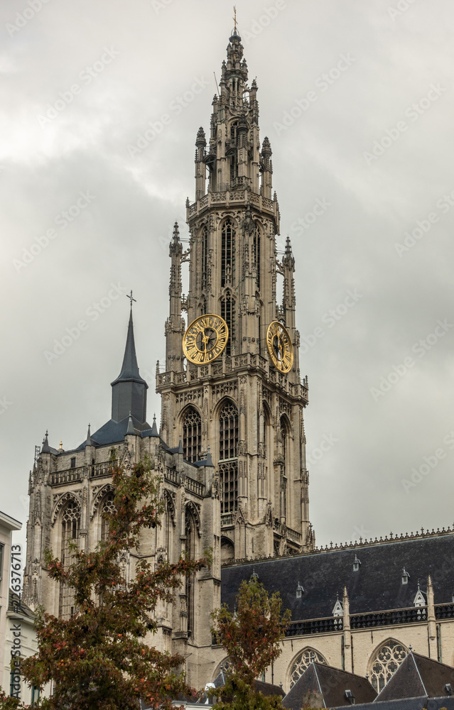 Antwerp, Belgium - September 24, 2018: Closeup of Towers and nave of Onze-Lieve-Vrouwe Cathedral of Our Lady in back under gray cloudy sky. Some green foliage.