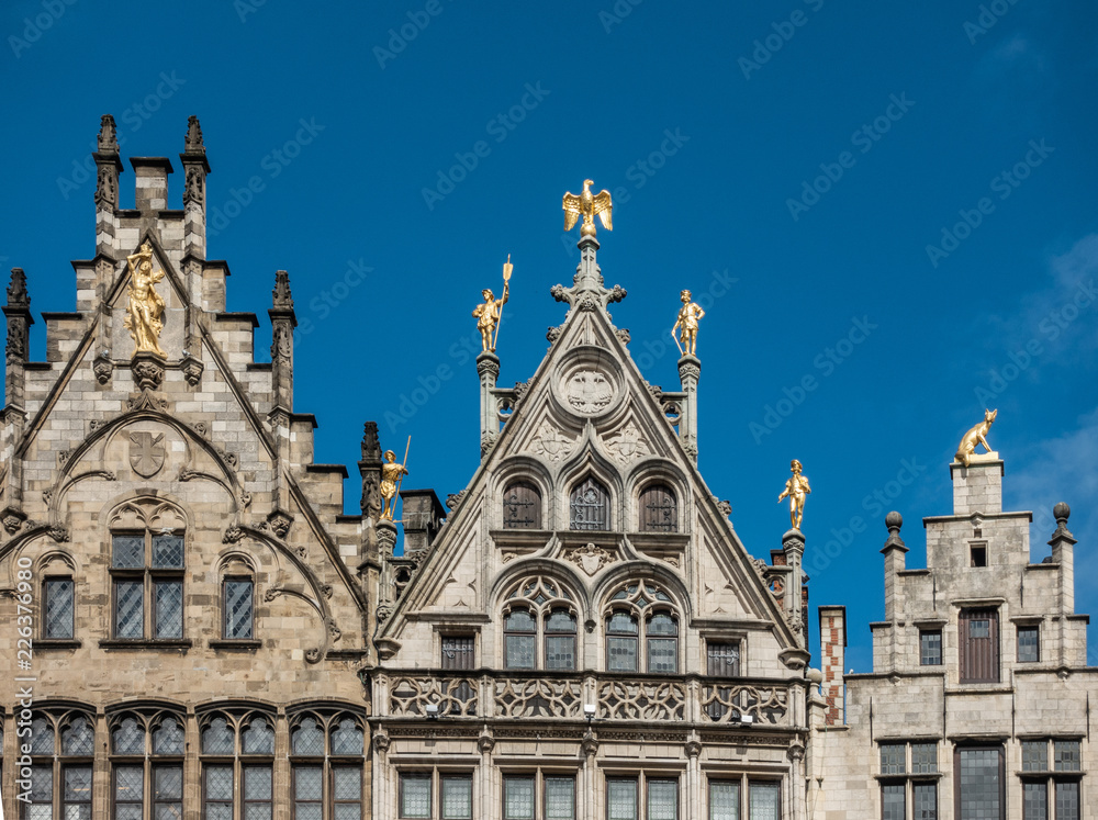 Antwerp, Belgium - September 24, 2018: Golden statues on top of the facades of guild houses on Grote Markt. Brown stones, arches under blue sky.