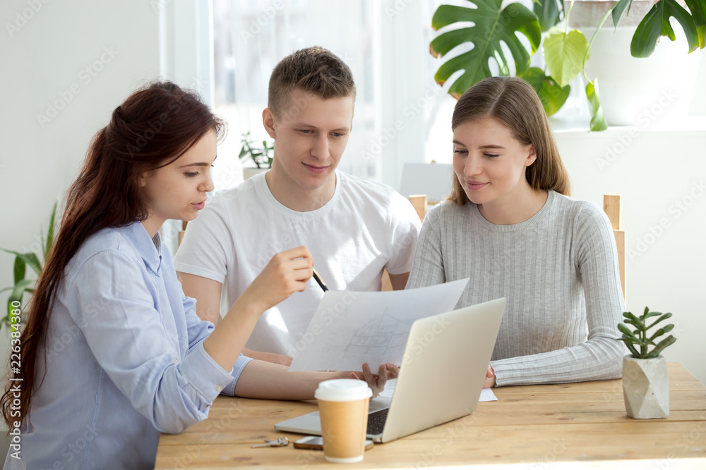 Happy married young millennial couple visiting real estate agency meets with realtor or architect. Agent worker female showing to customers clients building house architectural plan, renovation idea Happy married young millennial couple visiting real estate agency meets with realtor or architect. Agent worker female showing to customers clients building house architectural plan, renovation idea