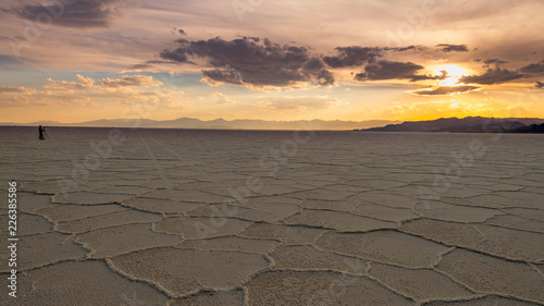 Spectator watches the sun set over the salt flats in Utah with car tracks in the salt