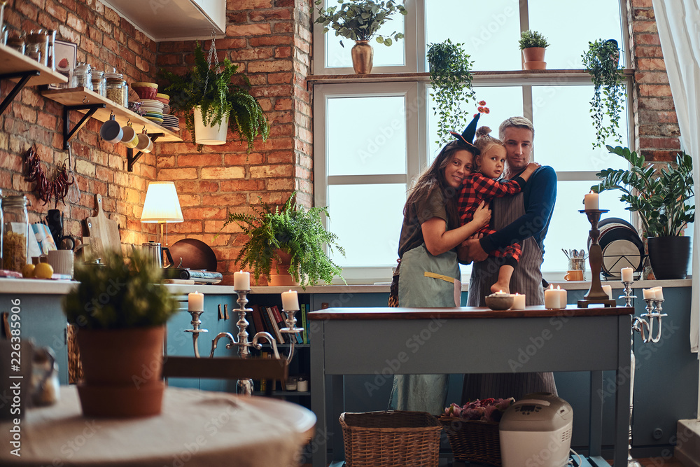 Mom dad and little daughter embracing together in loft style kitchen at morning.