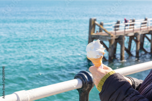 Womans Hands Holding an Ice Cream in a Cone With a Metal Rail and the Sea Beyond