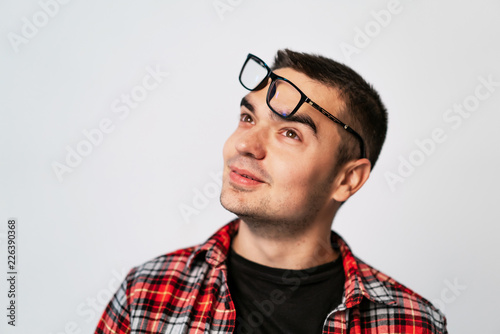 adult man in a plaid shirt and with raised glasses on his forehead looks up on a white background in the studio. Close-up © Vadim