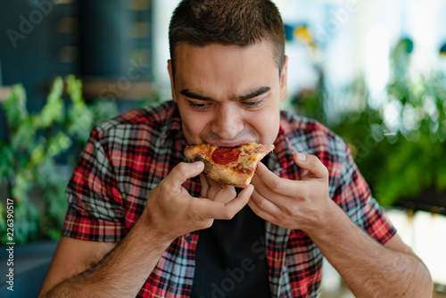 handsome man in a red plaid shirt is eats a pizza at a cafe. Hungry man eats a slice of hot pizza with cheese  sausage and sauce. Close-up