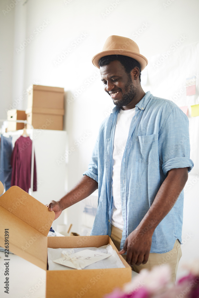Owner of modern fashion studio or atelier packing one of orders into box before sending it to client Owner of modern fashion studio or atelier packing one of orders into box before sending it to client