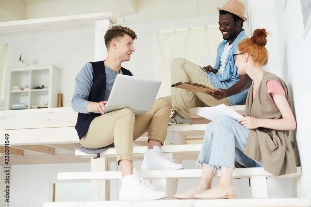 Obraz premium Group of creative intercultural designers sitting on staircase while brainstorming and discussing ideas