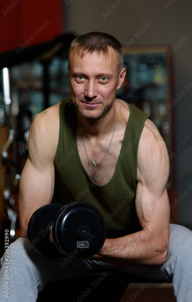 Confident young handsome man in sportswear, exercises with dumbbells in the gym.