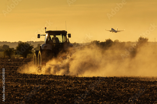 фотографія Modern tractor plowing at the sunset with lot of dust in background and with a p