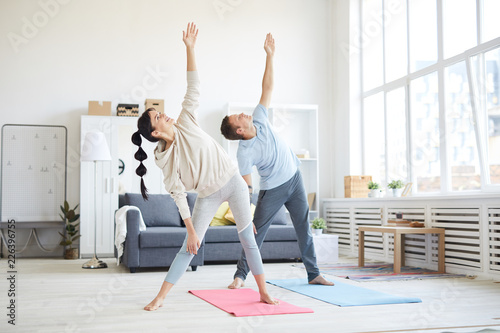 Young sporty couple in activewear raising their left arms while exercising in living-room at home