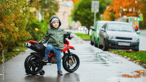 A beautiful little boy posing at his children s red motorcycle. The concept of teaching children to motor vehicles from an early age