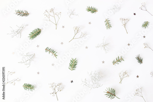 Christmas floral pattern. Winter composition of green spruce tree branches, baby's breath flowers, Calocephalus brownii and silver confetti stars on white table. Festive background. Flat lay, top view photo