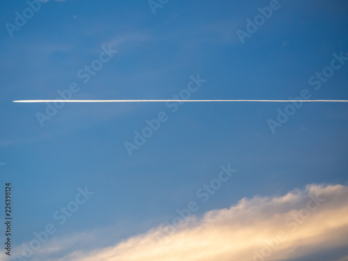 Trail of the plane against the blue sky and sunset clouds